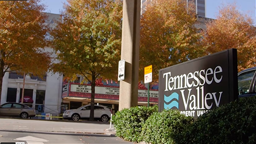 The front of a building outdoors with some trees. The front of the building shows the TVFCU logo.